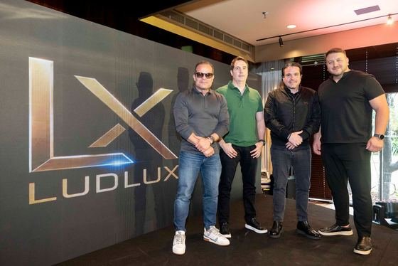 Equipe LudLux reunida diante do painel com a marca